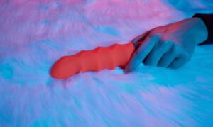 Uma Mulher Deitada Em Uma Cama, Segurando Um Vibrador Na Mão, Parecendo Relaxada E Envolvida Em Sua Intimidade.