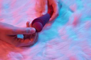 Uma Mulher Deitada Em Uma Cama, Segurando Um Vibrador Em Sua Mão, Explorando Sua Sexualidade.