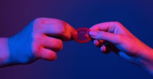Um Close Nas Mãos De Um Casal Segurando Um Preservativo, Simbolizando Paixão E Desejo Em Jogos Sexuais.