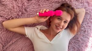 Uma Mulher Jovem E Feliz Deitada Em Uma Cama, Segurando Um Vibrador E Sorrindo, Representando Autoafirmação E Confiança.