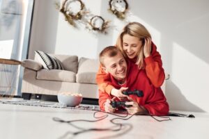 Um Jovem Casal Aproveitando Um Fim De Semana Divertido Em Casa, Sentados Juntos No Sofá E Jogando Videogame, Demonstrando Amor E Felicidade.