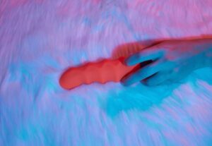 Uma Mulher Deitada Em Uma Cama, Segurando Um Dildo Realista Na Mão, Parecendo Relaxada E Envolvida Em Autoexploração.