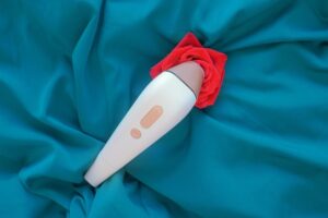 Um Close De Um Dispositivo De Sucção Clitoriana Em Formato De Rosa Vermelha Sobre Um Fundo De Cetim Verde, Destacando Seu Design Elegante Como Um Brinquedo Sexual.