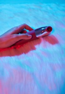 Uma Mulher Deitada Em Uma Cama, Segurando Um Vibrador Na Mão, Parecendo Relaxada E Envolvida Em Auto-prazer.