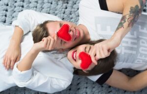 Um Casal Sorrindo E Segurando Corações De Brinquedo Vermelhos Perto Dos Rostos, Simbolizando Amor E Intimidade.