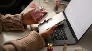 Mulher Segura Uma Garrafa De Perfume Enquanto Usa Um Smartphone Em Uma Mesa De Escritório.