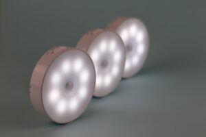 Três Luzes Noturnas De Led Translúcidas, Redondas, Sobre Uma Prateleira Do Banheiro.