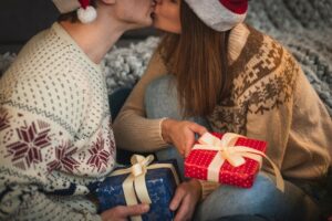 Primeiro Plano De Um Casal Se Beijando, Com Presentes De Natal Por Perto.