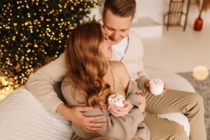 Casal Se Abraça E Relaxa Ao Lado De Uma áRvore De Natal Decorada, Dentro De Casa.